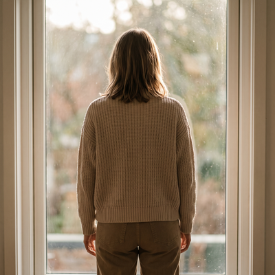 A person standing at a window in a sand knit